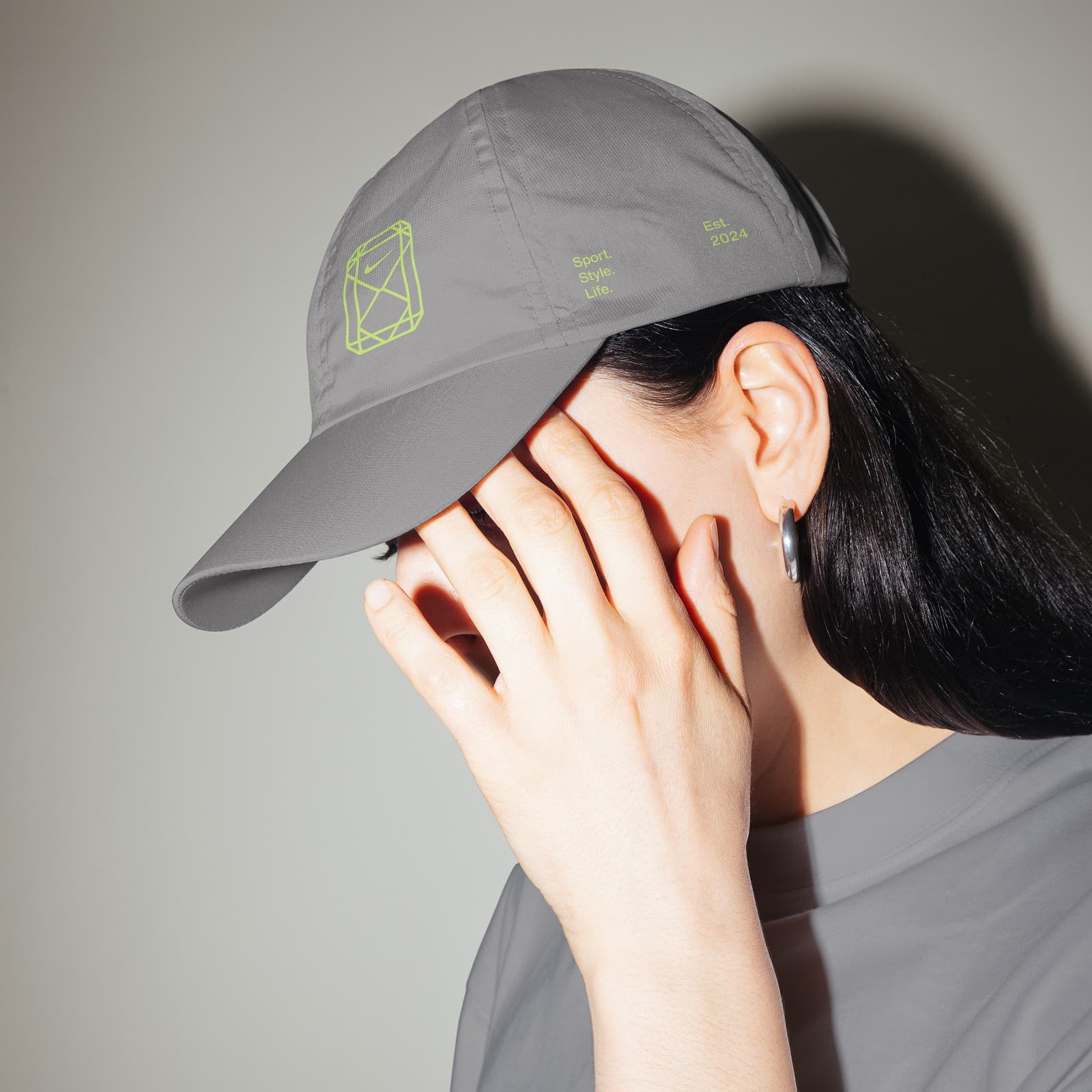 Grey cap with the gemstone mark, worn by a woman covering her face with her hand